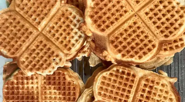 Nygräddade, gyllene glutenfria våfflor ligger staplade på ett galler. Perfekta för en fika!