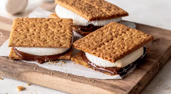 Drei S'mores Cookies mit geschmolzener Schokolade und Marshmallows auf einem Holzbrett.