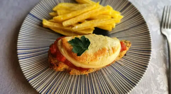 Delicioso pollo a la parmesana con papas fritas crujientes, servido en un plato rayado.