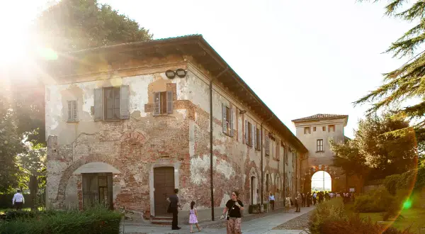 Passeggiata serale all'abbazia di Chiaravalle, con edifici storici in mattoni e un arco d'ingresso illuminato dal sole.