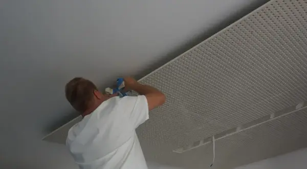 Mężczyzna montuje płyty karton gips na suficie w nieogrzewanym domu.