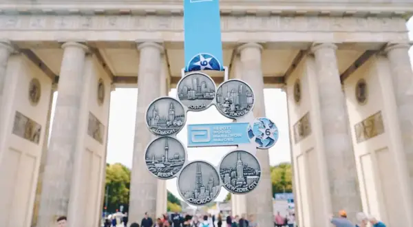 Medal za ukończenie korony maratonów świata przed Bramą Brandenburską. Widoczne miasta: Boston, Tokio, Nowy Jork, Chicago, Berlin, Londyn.