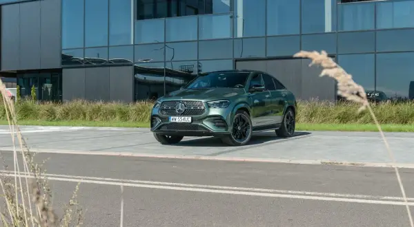 Zielony Mercedes-Benz GLE 450d coupe zaparkowany przed nowoczesnym budynkiem z lustrzanymi oknami.