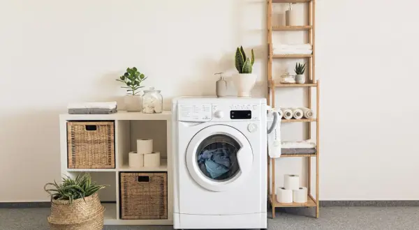 Waschmaschine mit Aquastop, die undicht ist, steht neben einem Regal mit Handtüchern und Pflanzen.