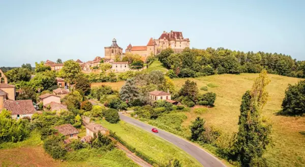Un village pittoresque en France, idéal pour savoir où partir en France en mai. Un château domine la colline verdoyante.