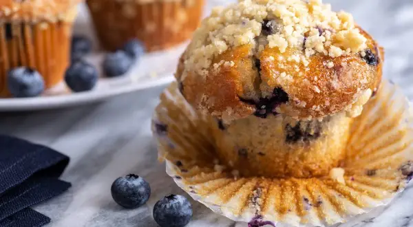 Saftige Blaubeermuffins mit Streuseln, perfekt für ein Blaubeermuffins Rezept. Frische Blaubeeren liegen daneben.