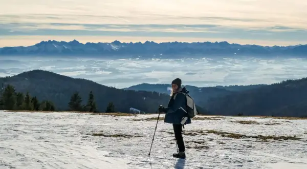 Kobieta z kijkami trekkingowymi na ośnieżonym szczycie, podziwiająca Tatry. To najładniejsza trasa na Turbacz zimą.