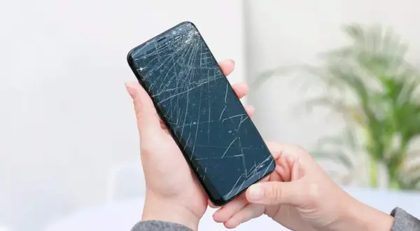 Dwie dłonie trzymają pęknięty telefon, czekając na wymianę dotyku.