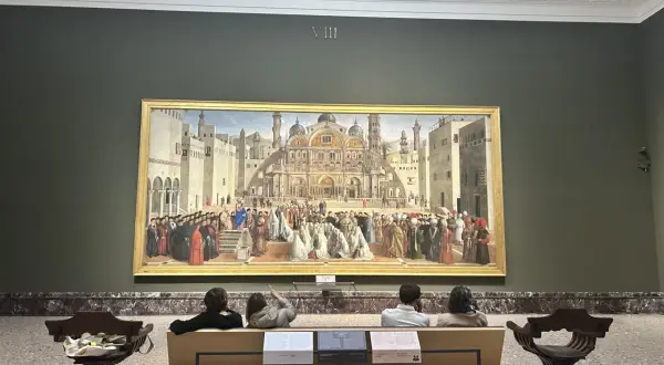 A grand painting depicting a historical scene is the centerpiece of this art in Milan gallery. Visitors sit on a bench, contemplating the detailed artwork.