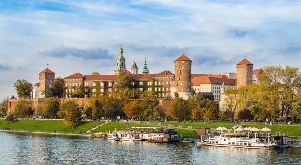 Zamek Królewski na Wawelu, majestatyczna budowla nad Wisłą, otoczona jesienną zielenią i błękitem nieba.