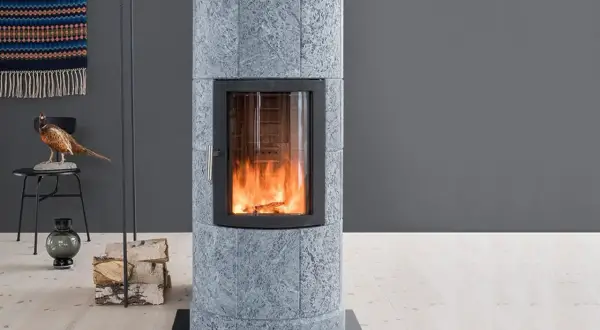 Poêle en pierre ollaire aux flammes vives, avec une décoration de faisan et de bois de chauffage à proximité.