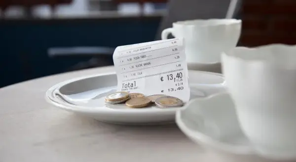 Rechnung mit Münzen auf einem Teller, bereit für das Trinkgeld nach dem Essen auf Sardinien.