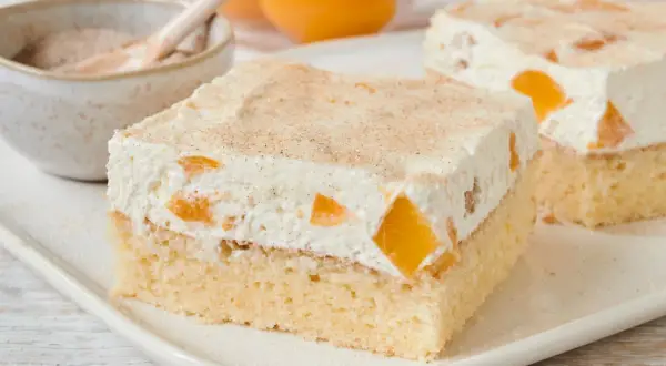 Saftiger Pfirsich Schmand Kuchen mit zarter Sahne und Zimt bestreut. Ein Genuss für jeden Anlass.