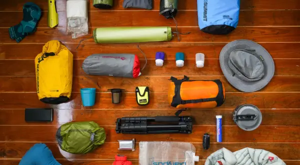 A collection of gear for a backpacking trip: dry bags, sleeping pad, socks, hat, first aid kit, water bladder, and more.