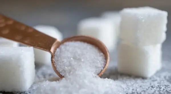 Łyżeczka z kryształkami, obok kostki cukru. Czy to sorbitol? Ten słodzik jest często używany jako zamiennik cukru.