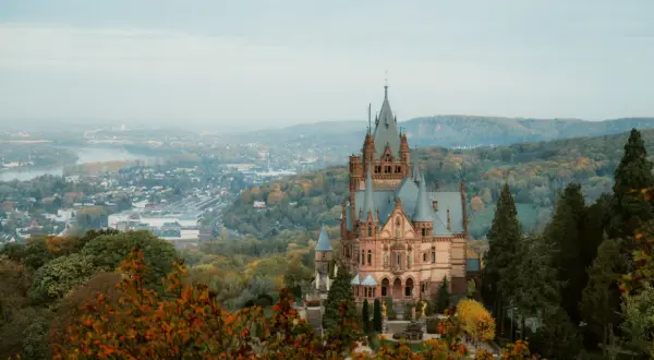 Märchenschloss im Herbstlicht, ein Juwel unter den Burgruinen NRW, thront über einer nebligen Stadt und einem Fluss.