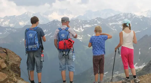 Familie genießt die Aussicht bei einer Bergtour mit Kindern. Die beeindruckende Berglandschaft erstreckt sich bis zum Horizont.