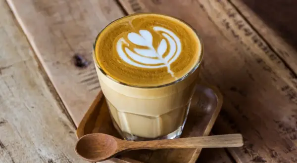En vacker caffe latte med latte art på ett träbord. En träsked ligger bredvid.