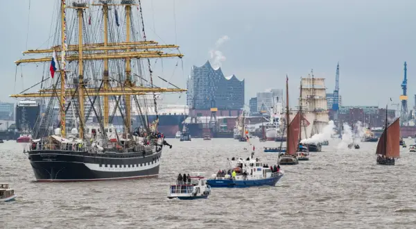 Große Segelschiffe und Dampfer nehmen an der einlaufparade hafengeburtstag teil, mit der Elbphilharmonie im Hintergrund.