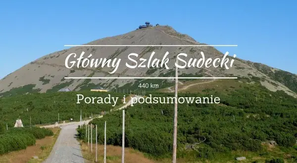 Główny Szlak Sudecki, 440 km. Widok na górę ze szczytem i budynkami, droga kamienista, zieleń.