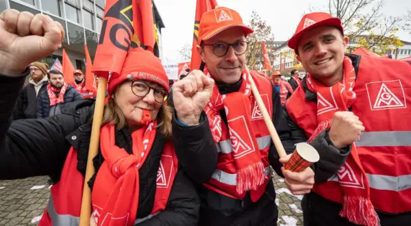 Drei Personen in roten Westen und Schals mit Gewerkschaftssymbolen, die Fahnen schwenken und die Faust ballen.