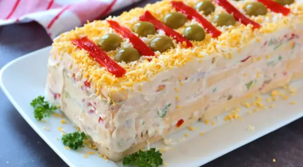 Pastel de atún con pan de molde, decorado con pimientos rojos, aceitunas y huevo rallado. ¡Una delicia!