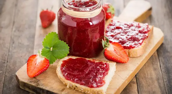 Confiture de fraises sur pain grillé, un délice qui peut faire grimper le cholestérol. Fraises fraîches et une feuille verte sur fond de bois.