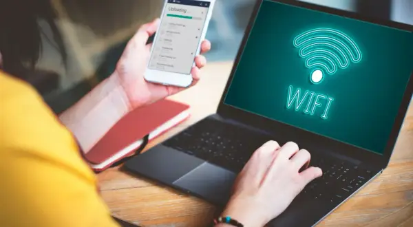 Osoba korzysta z telefonu i laptopa, na ekranie którego widnieje symbol Wi-Fi. Możliwość wi-fi calling Orange ułatwia pracę zdalną.