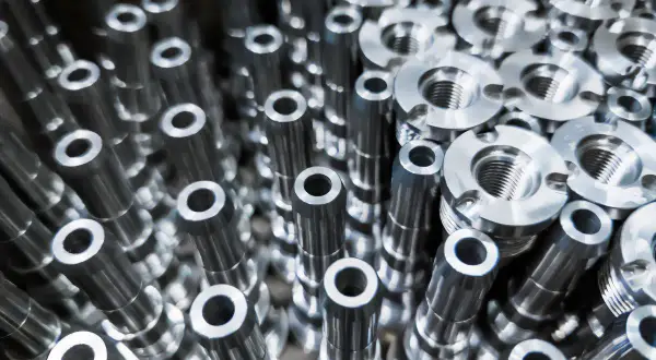 Metalowe elementy, precyzyjnie wykonane przez toczenie CNC, tworzą gęsty wzór. Widać gwintowane części i cylindryczne detale.