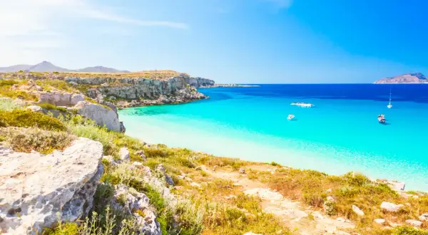 Paesaggio mozzafiato con le calette di Favignana, acque cristalline e barche all'ancora.