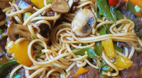 Pyszny makaron chow mein z wołowiną, pieczarkami, papryką i groszkiem cukrowym w sosie.