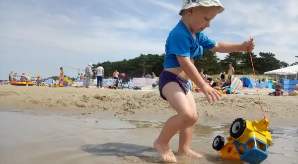 Chłopiec ciągnie zabawkowe auto po plaży w Darłowie. To świetne darłowo atrakcje dla dzieci, gdzie można się bawić w wodzie i piasku.