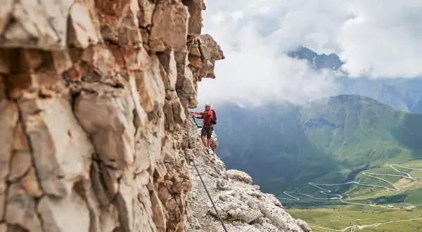 Wspinacz na via ferrata w Dolomitach, z widokiem na kręte drogi i zielone doliny.