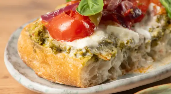 Bruschetta au pesto, tomates fraîches, mozzarella fondante et oignons rouges sur une tranche de pain grillé. Un délice !