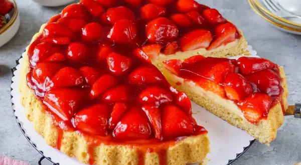 Eine saftige Erdbeertorte mit frischen Erdbeeren und Tortenguss, ein Stück wird herausgeschnitten.