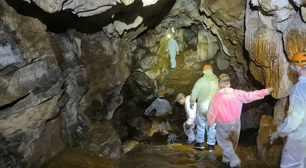 Exploradores descienden en la Cova do Rei Cintolo, iluminando formaciones rocosas y charcos de agua.