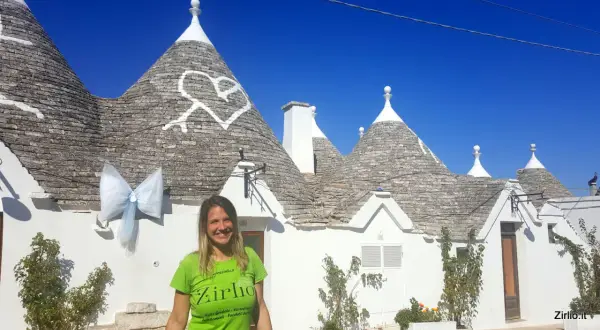Una donna sorride davanti ai trulli di Alberobello, patrimonio UNESCO, con un grande fiocco azzurro appeso a un cono.