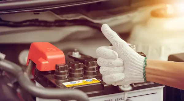 Main tenant, une main gantée fait un pouce levé près de la batterie d'une voiture qui a du mal à démarrer diesel.