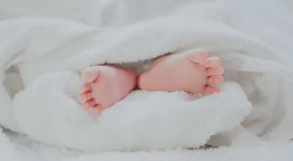 Petits pieds roses d'un bébé, emmitouflés dans une couverture blanche. Quel jour pour un baptême, une nouvelle vie commence !
