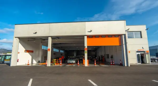 Estación de ITV con coches esperando para pasar la inspección. Un conductor decide pasar la ITV antes de tiempo para evitar multas.