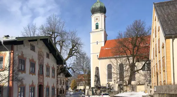 Winterliche Szene in Oberammergau mit der Pfarrkirche St. Peter und Paul. Die Fassadenmalerei der Häuser und die schneebedeckten Wege lassen die Vorfreude auf die passionsfestspiele oberammergau spüren.