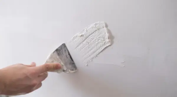 Dłoń z kielnią nakłada gips szpachlowy na białą ścianę.