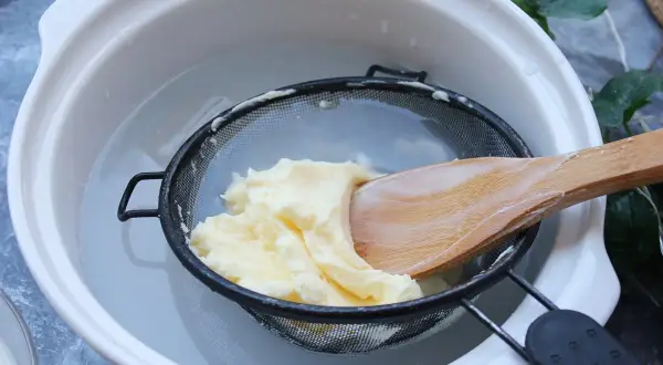 Proceso para como hacer mantequilla casera: se lava la mantequilla recién hecha en un colador con agua fría, usando una cuchara de madera.