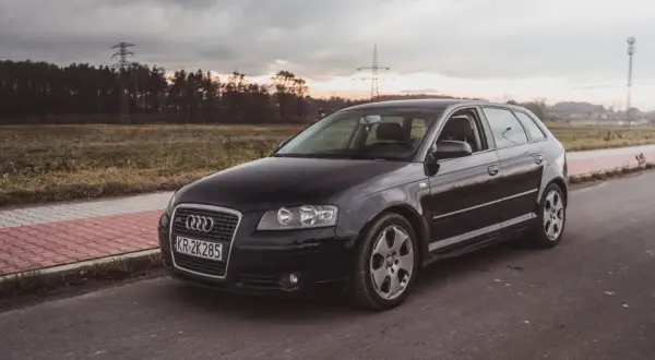 Czarne Audi A3 2009 na tle zachodzącego słońca i linii energetycznych.