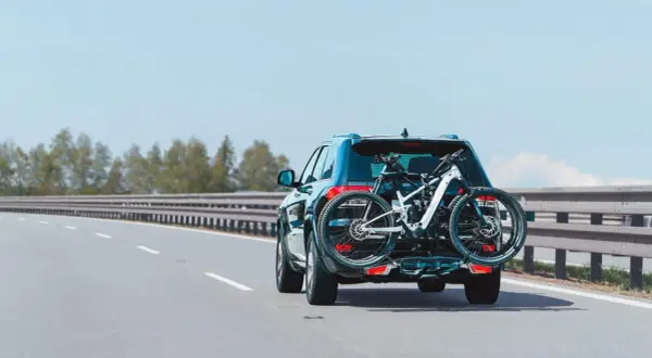 Un turismo transporta una bicicleta de montaña en un portabicicletas trasero. La carga sobresale considerablemente, pero es una forma común de llevar equipo deportivo.