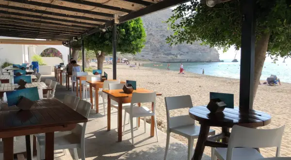 Mesas y sillas en el exterior del restaurante Agua Amarga, con la playa y el mar de fondo.