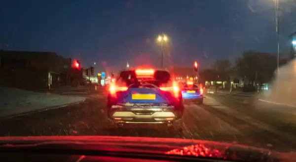 Noche de nieve, luces rojas de freno y un coche azul con matrícula amarilla. El asfalto mojado y la baja visibilidad aumentan el riesgo de derrape coche.