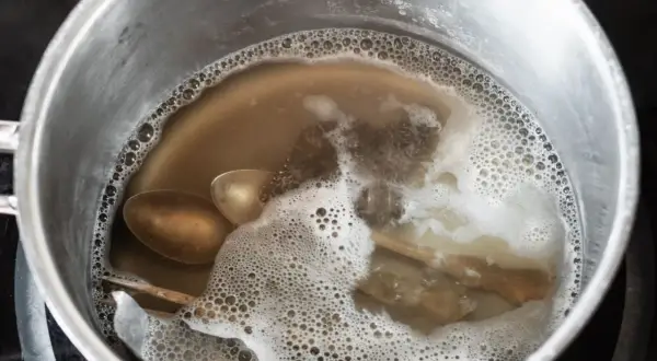 Srebrne łyżki i folia aluminiowa w garnku z bulgoczącą wodą.