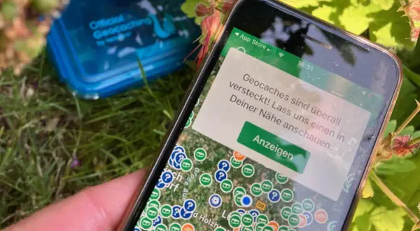 Smartfon pokazuje mapę z zaznaczonymi skrytkami. To jest właśnie geocaching – poszukiwanie ukrytych skarbów.