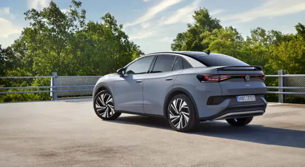 El Volkswagen ID.5 gris, con su diseño deportivo, se detiene en un día soleado, rodeado de árboles verdes y un cielo azul.
